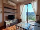 Modern living room with glass coffee table, wall-mounted TV, and a large sliding door opening to a balcony.