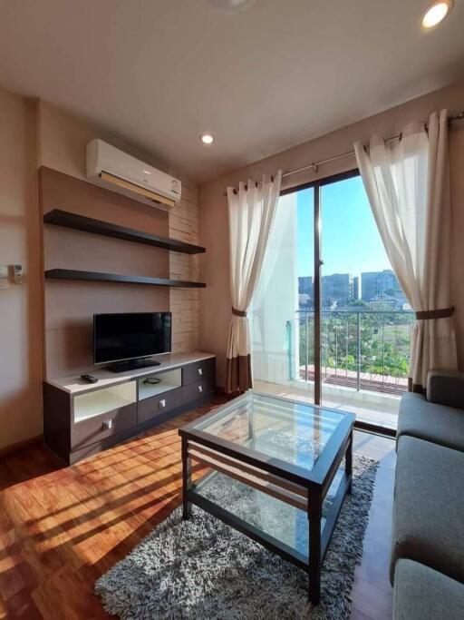 Modern living room with glass coffee table, wall-mounted TV, and a large sliding door opening to a balcony.