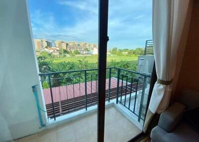 View of a balcony with railing, overlooking a green field and buildings in the distance