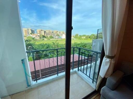 View of a balcony with railing, overlooking a green field and buildings in the distance