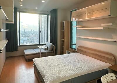 Modern minimalist bedroom with bed, shelves, large window, and a small seating area