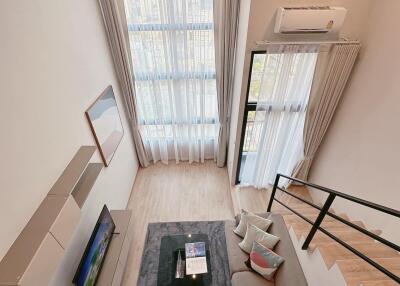 Modern living room with large window, loft view, TV unit, sofa, and stairs