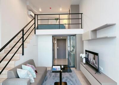 Modern living room with a mezzanine, featuring a couch, rug, TV, and staircase.