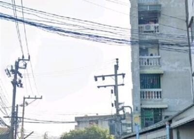 Street view of a building with visible balconies, electrical poles, and motorcycles parked on the street.