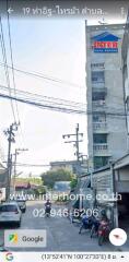 Street view of a building with visible balconies, electrical poles, and motorcycles parked on the street.