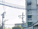 Street view of a building with visible balconies, electrical poles, and motorcycles parked on the street.