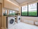 Modern laundry room with washer and dryer, cabinets, and large window