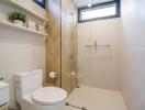 Modern bathroom with glass shower, toilet, and wall shelf