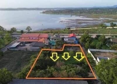 Aerial view of a land lot near a water body with three downward yellow arrows marking the boundary