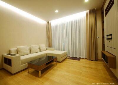 Modern living room with a sectional sofa, coffee table, wooden flooring, and floor-to-ceiling curtains