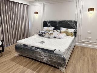 A bedroom with a large bed, decorative wall lights, and hardwood floor.