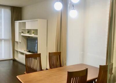 Dining area with wooden table and chairs, adjacent to living space with shelving unit