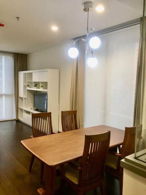 Dining area with wooden table and chairs, adjacent to living space with shelving unit