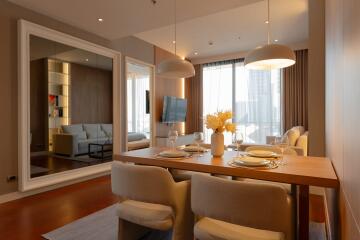 Modern dining room with a wooden table and elegant chairs, featuring a large mirror and open living space.