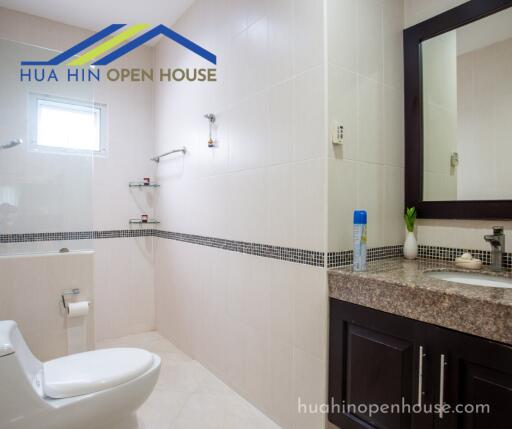 Modern bathroom with white tiles, a toilet, and a sink with a mirror