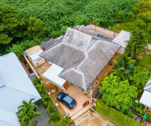 Aerial view of a residential house with lush greenery in the background