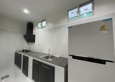 Modern kitchen with black cabinets, stainless steel sink, and a refrigerator.