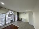 Spacious and bright living room with large arched window, white furniture, and grey flooring