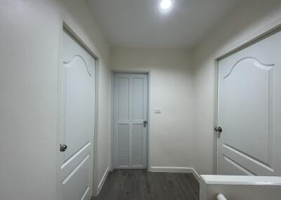 A well-lit hallway with three doors and wooden flooring