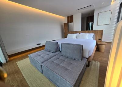 Modern bedroom with bed, upholstered bench, wood flooring, recessed lighting, and large window