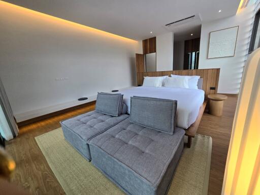 Modern bedroom with bed, upholstered bench, wood flooring, recessed lighting, and large window