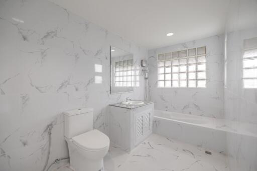 Modern white marble bathroom with built-in bathtub, toilet, modern sink, and large window blocks