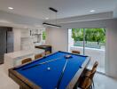 Modern living area with pool table and kitchen overlooking a garden