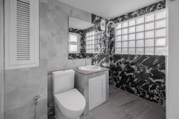 Modern bathroom with black and white marble shower wall, sink, toilet, and glass block window