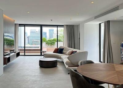 Modern living room with a sectional sofa, TV, dining table, large windows, and a city view