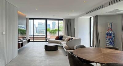 Modern living room with a sectional sofa, TV, dining table, large windows, and a city view