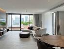 Modern living room with a sectional sofa, TV, dining table, large windows, and a city view