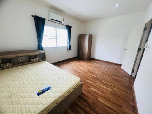 Spacious bedroom with wooden floors and a window with dark curtains