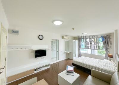 Bright and modern studio apartment with wooden flooring, bed, sofa, wall-mounted TV, and large window.