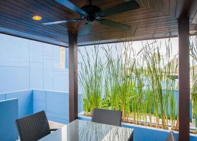 Modern outdoor patio area with glass table and wicker chairs under a wooden ceiling with a fan