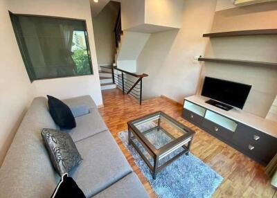 Modern living room with wooden floor, grey sofa, glass coffee table, TV, and staircase