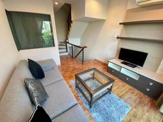 Modern living room with wooden floor, grey sofa, glass coffee table, TV, and staircase