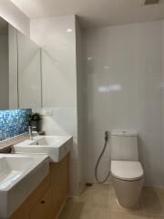 Modern bathroom with dual sinks, blue mosaic tile accents, and a toilet