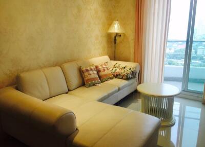 Cozy living room area with cream-colored sectional sofa and decorative pillows near a window with a city view.