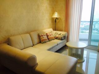 Cozy living room area with cream-colored sectional sofa and decorative pillows near a window with a city view.