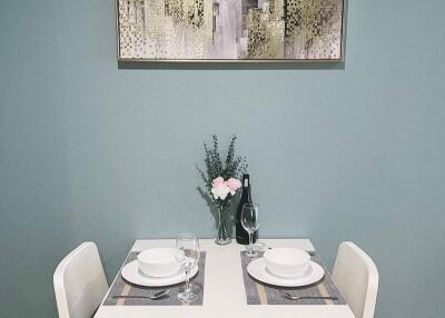 Small dining area with table setup for two, decorated with painting and flower vase.