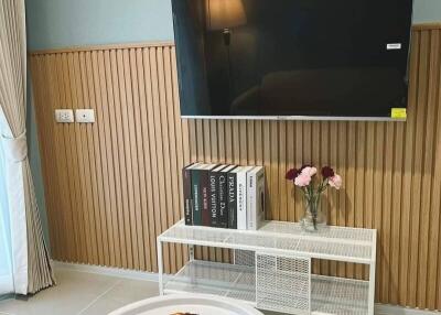 Modern living room with wall-mounted TV, small table with coffee and pastries, books, and flowers