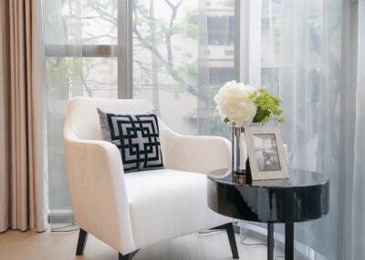 Stylish living room corner with a white armchair, decorative pillow, small black round table, and large window.