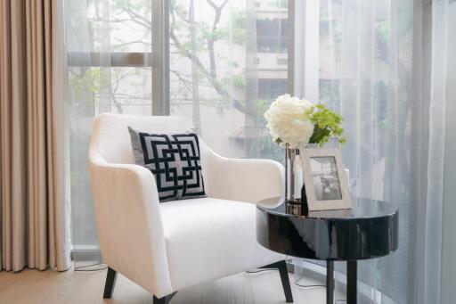 Stylish living room corner with a white armchair, decorative pillow, small black round table, and large window.