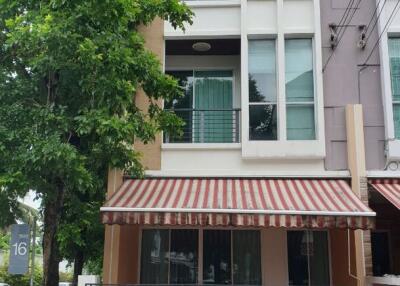 Exterior view of a three-story residential building with balconies and a striped awning