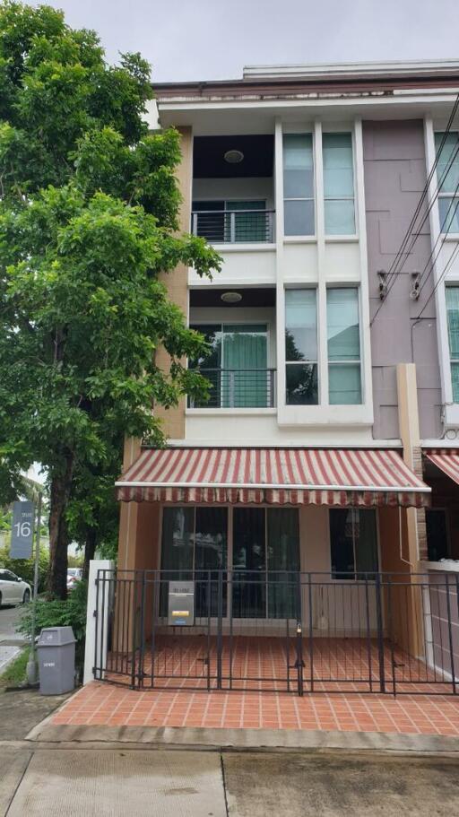 Exterior view of a three-story residential building with balconies and a striped awning