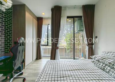 Modern bedroom with a checkered bedspread, a gaming chair, large windows, balcony view, and wardrobe.