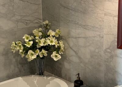 Bathroom with marble tiles, a bathtub, a vase with flowers, and a sink