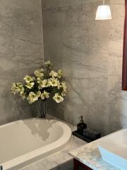 Bathroom with marble tiles, a bathtub, a vase with flowers, and a sink