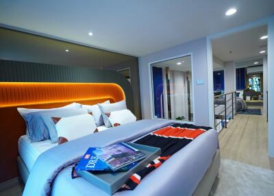 Modern bedroom with decorative pillows and bedspread, featuring a view into another bedroom through a glass partition.