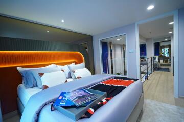 Modern bedroom with decorative pillows and bedspread, featuring a view into another bedroom through a glass partition.